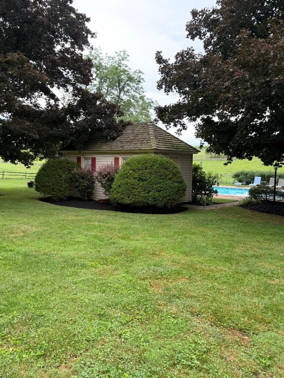 Broad foreground lawn with trimmed shrubs around a small outbuilding